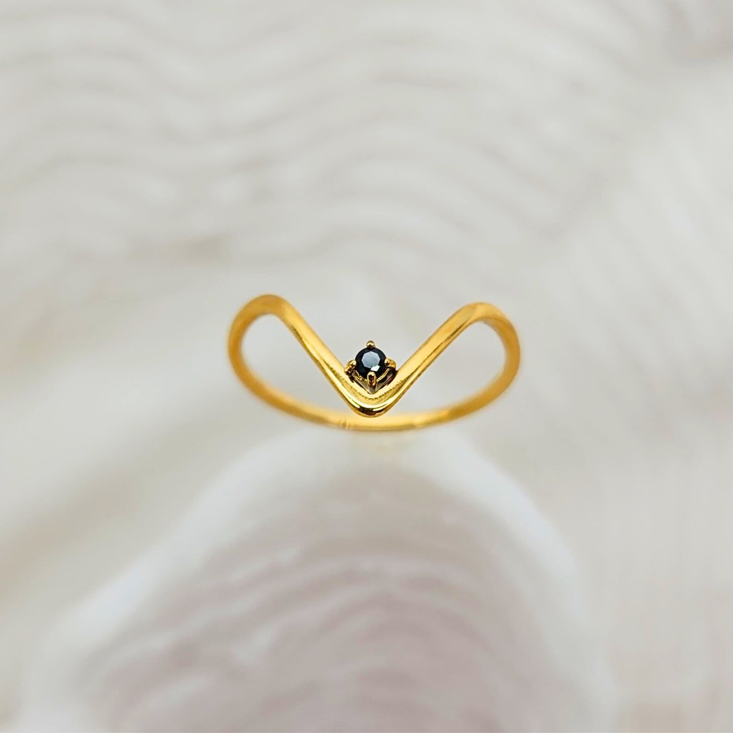Dainty gold V ring with centered black onyx stone against soft neutral background