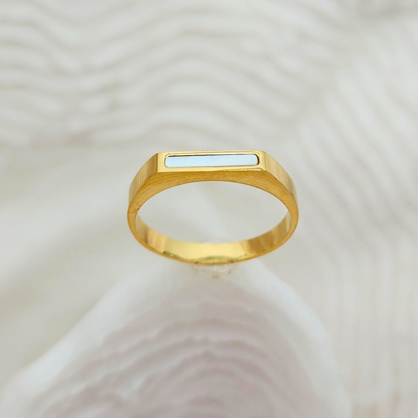 Minimalist gold bar ring with glossy white seashell inlay on textured background