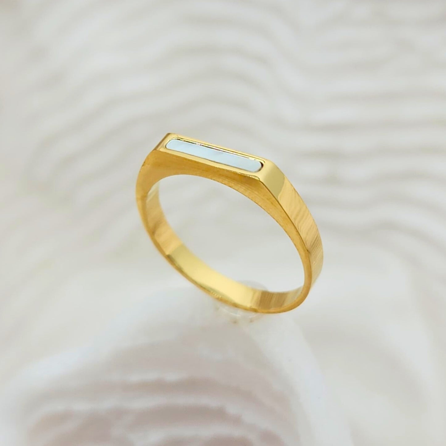 Angled view of gold seashell bar ring with smooth white inlay and matte finish band