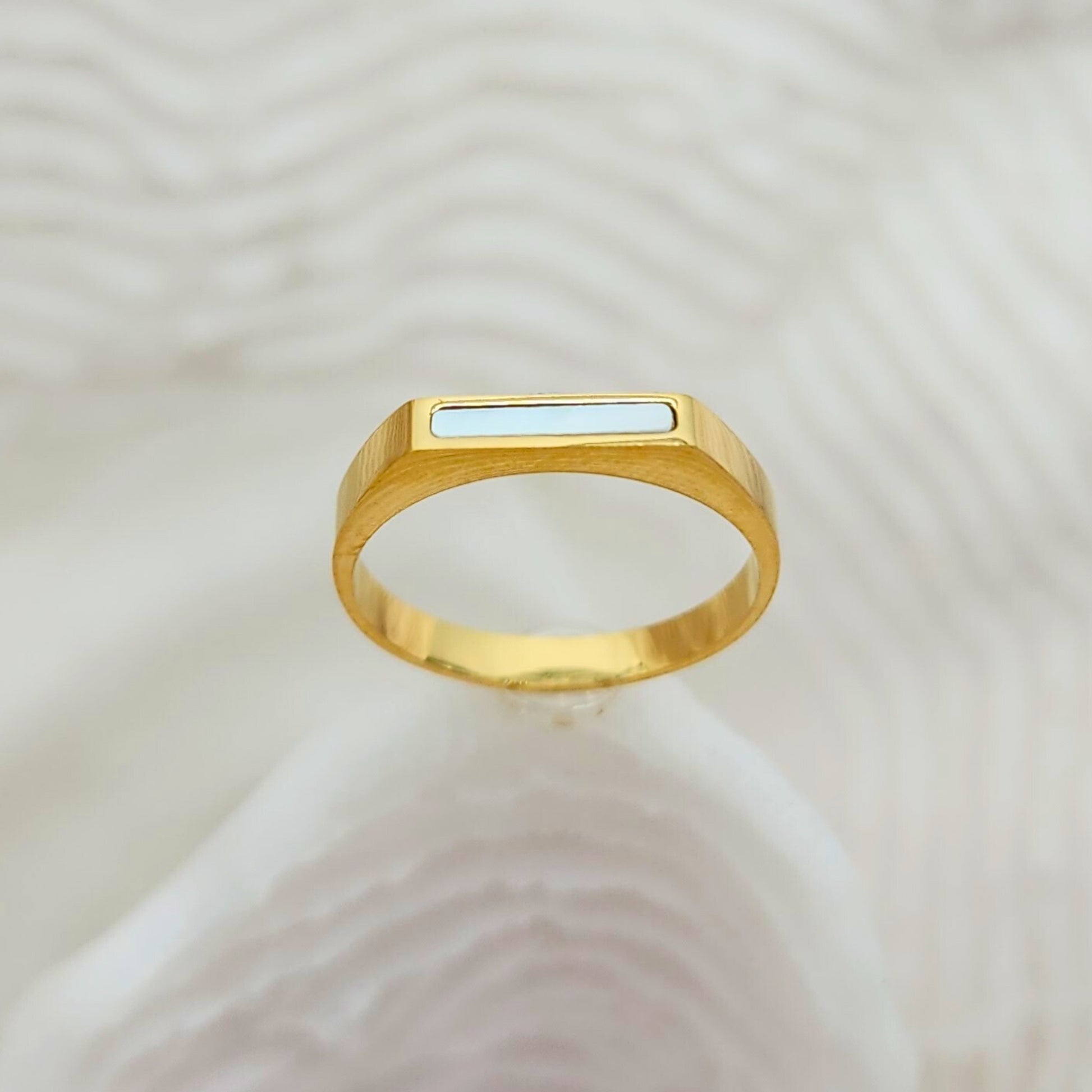 Minimalist gold bar ring with glossy white seashell inlay on textured background