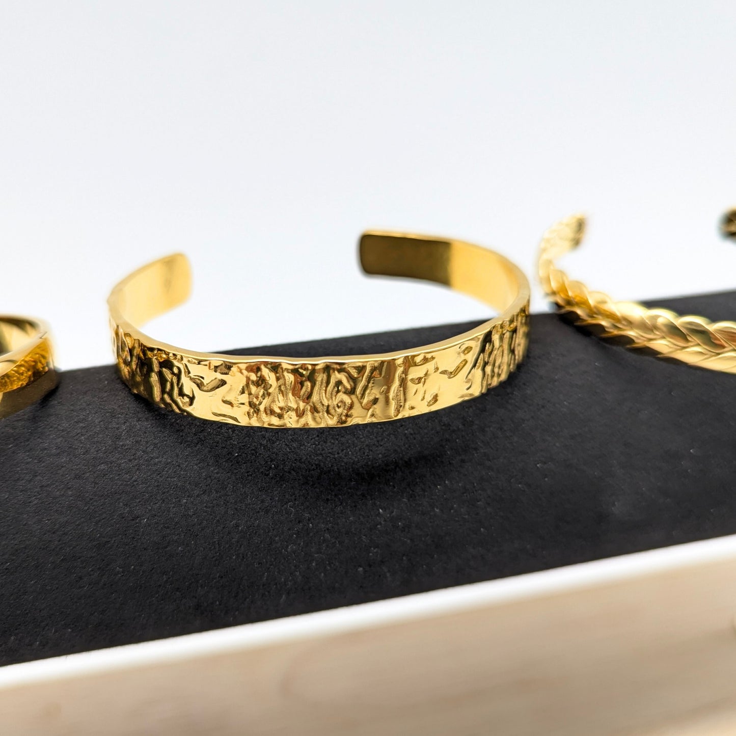 Gold bracelets on a black stand with a white background